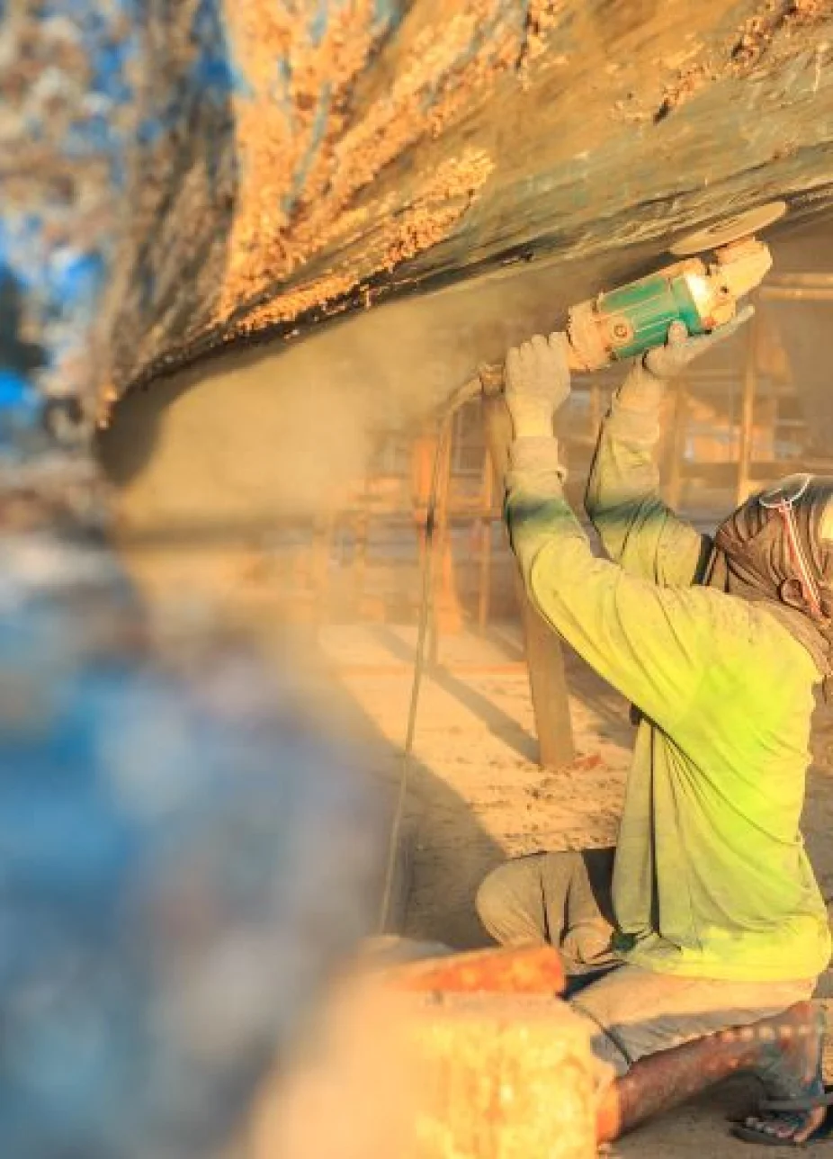 Worker removing paint from hull of ship